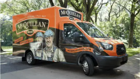 Orange and black McQuillan Bros service van, showcasing illustrations of two people, offers General Heating Repair services. With trees lining the background, this vehicle is ready to tackle any heating challenge with expertise and efficiency.