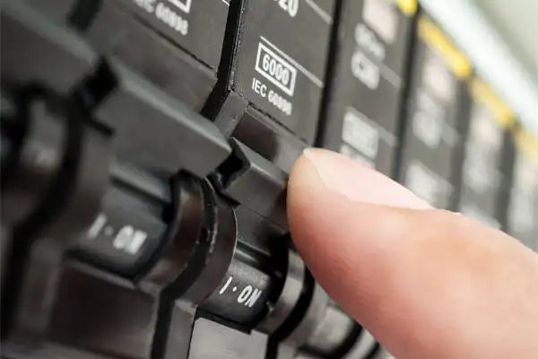 A finger is pressing a switch on a circuit breaker panel, labeled "6000 IEC 60898," during the circuit breaker installation process.
