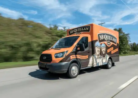 A McQuillan-branded van, highlighting General Heating Repair, drives on a highway with trees in the background. The van proudly displays graphics and a logo on its side.