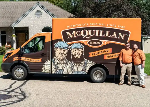 Two people in matching orange shirts stand beside a McQuillan Bros plumbing and heating van with a vintage-style design in a residential area, ready for their next General Heating Repair service.