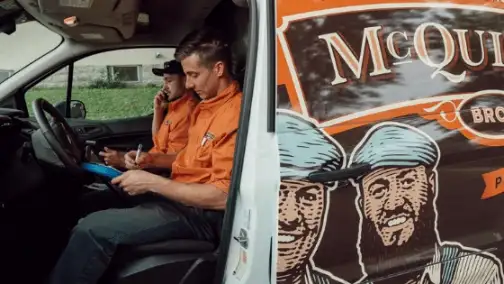 Two men in orange shirts sit inside a white vehicle. One writes on a clipboard, while the other talks on the phone about General Heating Repair. A graphic of two men in hats adorns the door, highlighting their expertise.