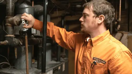 A person in an orange shirt meticulously inspects and adjusts a valve on a complex set of industrial pipes, showcasing their expertise in general heating repair.