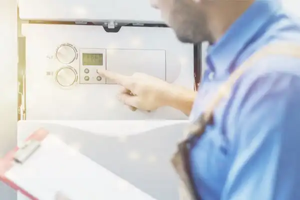 A person in a blue shirt adjusts the settings on a wall-mounted control panel while holding a clipboard, ensuring the tankless water heater installation is perfect.