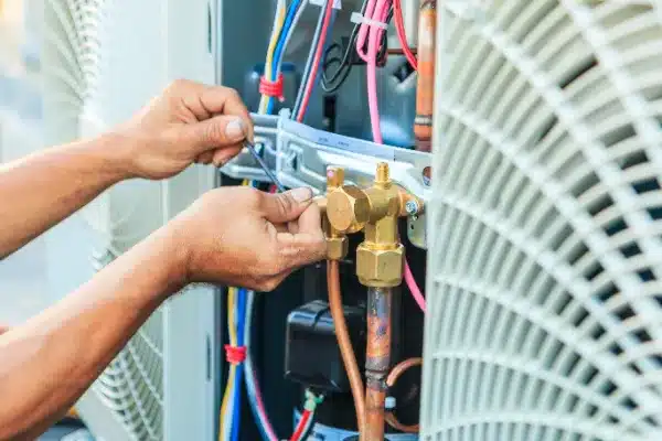 Person's hands diligently adjusting connections on an HVAC unit with a wrench, showcasing the nuanced art of air conditioning maintenance. Colorful wires intertwine with gleaming brass fittings, reflecting the meticulous attention required for optimal performance.